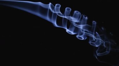 Duman, karmaşık spiral şekillerde soldan sağa doğru akar. Beyaz duman, siyah arka planda ağır çekimde uzayda süzülür. Kapat..