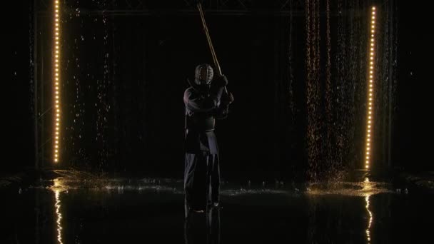 Japonský bojovník Kendo v bojovém postoji bodá Shinaiem. Muž v tradičním bojovém brnění a s bambusovým mečem cvičí bojové dovednosti na pozadí černého studia a deště. Zpomalený pohyb. — Stock video