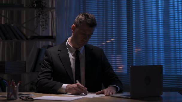 Бізнесмен перевіряє, підписує ручкою контракт. Бос у костюмі сидить за столом у вечірньому офісі. Підписання робочих паперів, угод або угод, погодження партнерства. Повільний рух готовий, 4K на 59.94fps . — стокове відео
