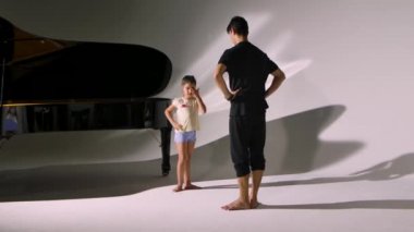 Küçük kız için kişisel bale dersi. Profesyonel öğretmen balerine dans öğeleri öğretiyor. Piyanonun yanında beyaz bir stüdyoda öğretmeniyle bir çocuğun bireysel uygulaması..