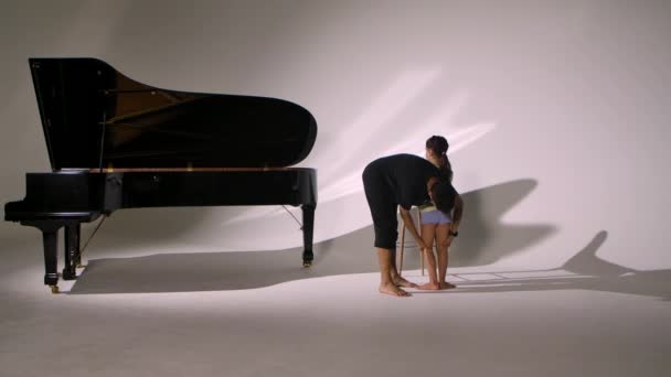 Personal ballet lesson for little girl. Professional teacher teaches child elements of dance and corrects positioning legs and stretching. Diligent ballet student trains on white studio background. — Stock Video