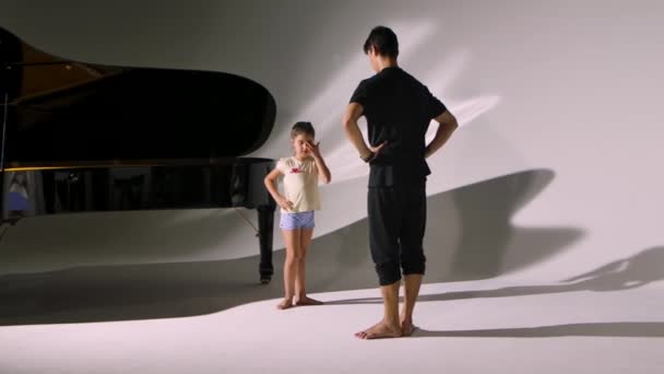 Persönliche Ballettstunde für kleines Mädchen. Professioneller Lehrer bringt der Ballerina Tanzelemente bei. Individuelles Üben eines Kindes mit einem Lehrer auf weißem Studiohintergrund in der Nähe des Klaviers. — Stockvideo