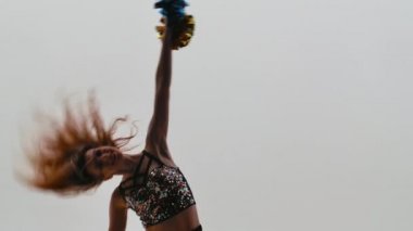 İnce ponpon kız silueti parlak bluzlu ve ponponlar ellerinde beyaz stüdyo arka planında enerjik bir şekilde dans ediyor. Spor müsabakalarında amigoluk. Kapatın. Yavaş çekim.