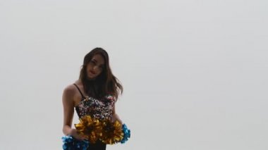 İnce ponpon kız silueti parlak bluzlu ve ponponlar ellerinde beyaz stüdyo arka planında enerjik bir şekilde dans ediyor. Spor müsabakalarında amigoluk. Kapatın. Yavaş çekim.