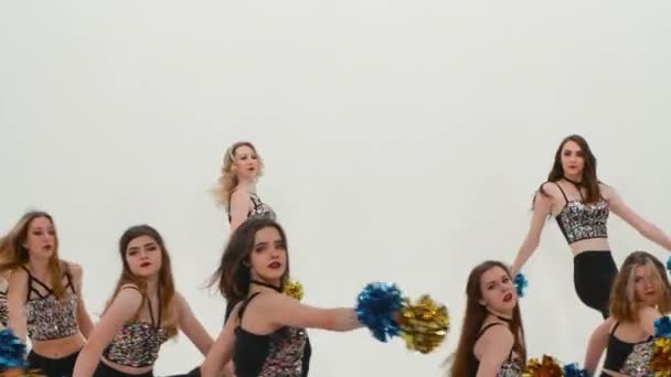 Groep atletische cheerleaders in zilveren tops en zwarte strakke leggings dansen juichende dans op witte studio achtergrond. Studenten dansen en zwaaien pompons synchroon in slow motion. Sluiten.. — Stockvideo