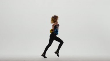 İnce ponpon kız silueti parlak bluzlu ve ponponlar ellerinde beyaz stüdyo arka planında enerjik bir şekilde dans ediyor. Spor müsabakalarında amigoluk. Yavaş çekim.