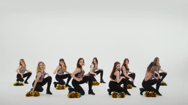 Eine Gruppe athletischer Cheerleader in silbernen Tops und schwarzen engen Leggings tanzt jubelnde Tänze auf weißem Studiohintergrund. Schüler tanzen und schwenken Bommel synchron in Zeitlupe. — Stockvideo