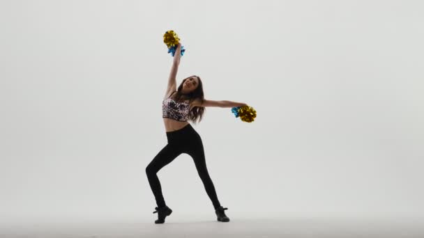 Silhueta de líder de torcida esbelta em topo brilhante e leggings que dançam energeticamente com pompons em mãos no fundo de estúdio branco. Dança animadora em competições desportivas. Movimento lento. — Vídeo de Stock