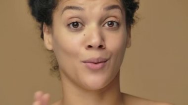 Genç Afrikalı Amerikalı bir kadının güzel portresi bir sürü ilginç bilgi veriyor ve anlatıyor. Kahverengi stüdyo arka planında poz veren siyah bir kadın model. Kapatın. Yavaş çekim hazır, 4K 59.94fps 'de..