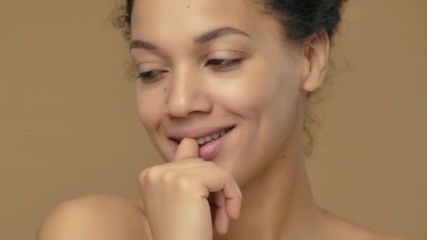 Portrait de beauté de jeune femme afro-américaine regardant coquettiquement la caméra et soufflant baiser. Modèle féminin noir posant sur fond de studio brun. Ferme là. Prêt au ralenti, 4K à 59.94fps. — Video