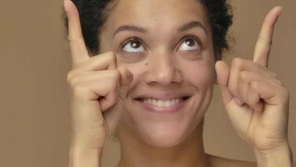 Szépségportré fiatal afro-amerikai nőről, aki feltartja a kezét valamiért, aztán bólogat és felmutatja a hüvelykujját. Fekete nő pózol barna stúdió háttérben. Közelről. Lassú mozgás kész, 4K 59.94fps-on. — Stock videók