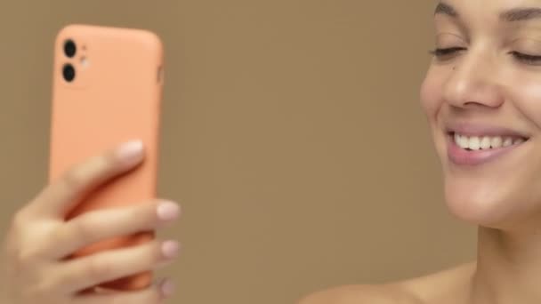 Portrait de beauté de jeune femme afro-américaine parle sur un appel vidéo à l'aide d'un smartphone. Modèle féminin noir posant sur fond de studio brun. Ferme là. Prêt au ralenti, 4K à 59.94fps. — Video