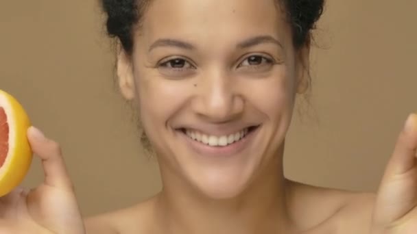 Πορτραίτο ομορφιάς μιας νεαρής Αφροαμερικανίδας που διασκεδάζει, καλύπτοντας τα μάτια με μισό γκρέιπφρουτ. Μαύρη γυναίκα σε φόντο καφέ στούντιο. Κλείσε. Αργή κίνηση έτοιμη, 4K στα 59.94fps. — Αρχείο Βίντεο