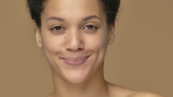 Retrato de belleza joven mujer afroamericana sosteniendo medio aguacate y crema facial, cuidado natural de la piel. Mujer negra sobre fondo de estudio marrón. De cerca. Cámara lenta lista, 4K a 59.94fps. — Vídeos de Stock