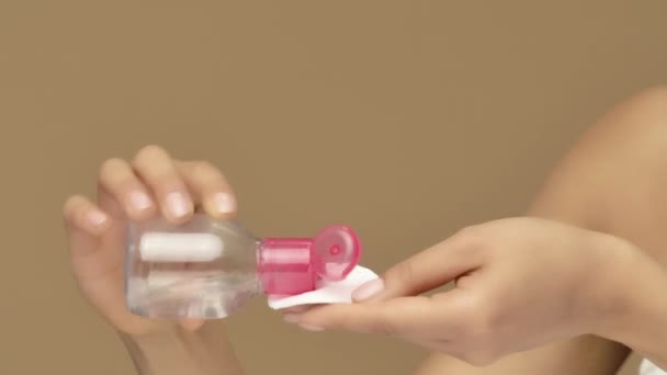 Beauty portrait of young African American woman pouring lotion onto cotton pad and cleansing face. Black female model posing on brown studio background. Close up. Slow motion ready, 4K at 59.94fps. — Stock Video