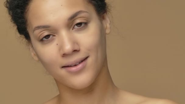 Beauty portrait of young African American woman twisting off a jar of cream and enjoying its aroma. Black female model posing on brown studio background. Close up. Slow motion ready, 4K at 59.94fps. — Stock Video