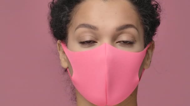 Portrait de beauté de jeune femme afro-américaine en masque pitta protecteur rose regardant la caméra. Modèle nu féminin noir posant sur fond de studio rose. Ferme là. Prêt au ralenti, 4K à 59.94fps. — Video