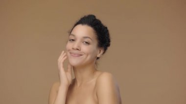 Afro-Amerikalı genç bir kadının güzel portresi kameraya bakıp öpüşüyor. Kahverengi stüdyo arka planında poz veren siyah bir kadın model. Yavaş çekim hazır, 4K 59.94fps 'de..