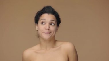 Afro-Amerikalı genç bir kadının omuz silkme ve şaşkın bakışlarla söylediği güzel bir portre. Kahverengi stüdyo arka planında poz veren siyah bir kadın model. Yavaş çekim hazır, 4K 59.94fps 'de..