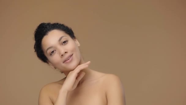 Retrato de belleza de una joven afroamericana, toca suavemente la cara con los dedos. Modelo femenino negro posando sobre fondo de estudio marrón. Cámara lenta lista, 4K a 59.94fps. — Vídeo de stock