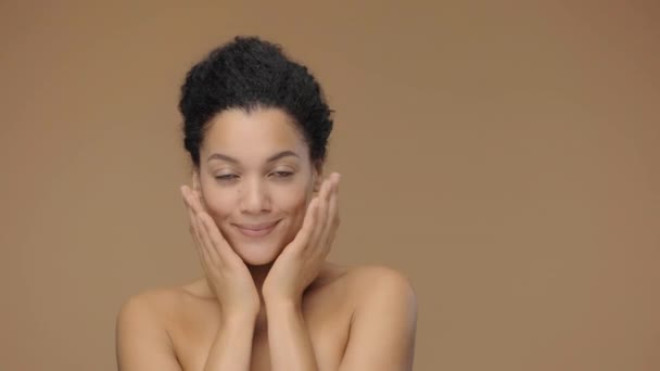 Retrato de beleza da jovem afro-americana rosto marcante com os dedos e dando massagem suave na pele. Mulher negra posando no fundo do estúdio marrom. Movimento lento pronto, 4K a 59.94fps. — Vídeo de Stock