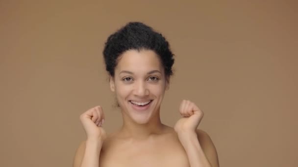 Красота портрет молодой афроамериканской женщины, улыбающейся и показывающей большие пальцы вверх жестом. Черная женщина позирует на фоне коричневой студии. Медленное движение готово, 4K на 59,94fps. — стоковое видео