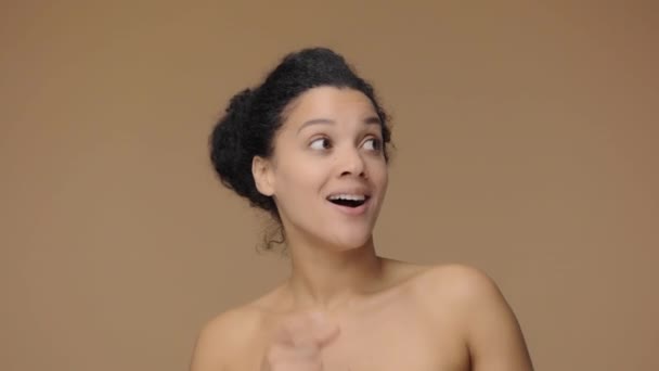 Retrato de belleza de una joven afroamericana apuntando con la mano para algo, asiente y muestra el pulgar como. Mujer negra posando sobre fondo de estudio marrón. Cámara lenta lista, 4K a 59.94fps — Vídeo de stock