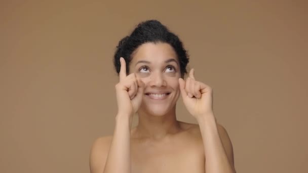 Skönhetsporträtt av ung afroamerikansk kvinna pekande upp handen för något sedan nickar och visar tummen upp. Svart kvinna poserar på brun studio bakgrund. Slow motion klar, 4K vid 59.94fps — Stockvideo