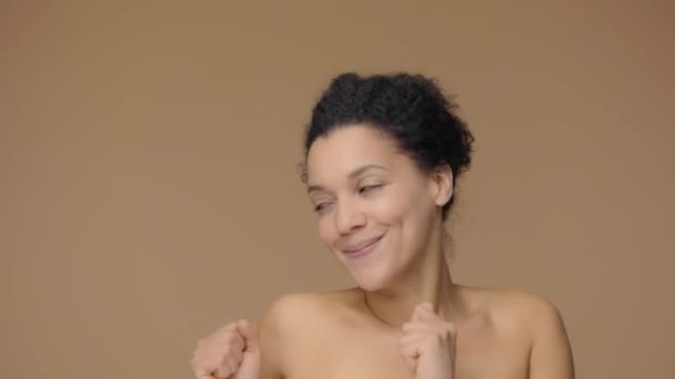 Skönhetsporträtt av ung afroamerikansk kvinna glatt dansande och leende. Lady med ren och slät hud. Svart kvinnlig modell poserar på brun studio bakgrund. Slow motion klar, 4K vid 59.94fps. — Stockvideo