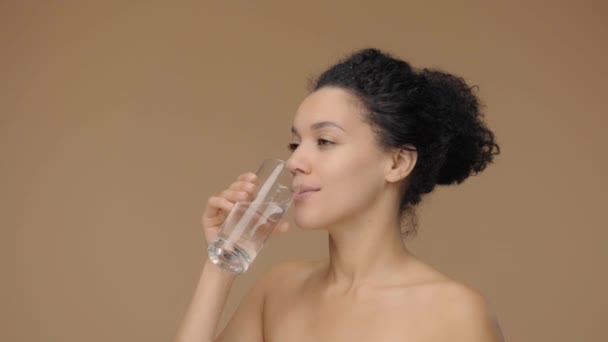 Ritratto di bellezza di giovane donna afroamericana beve acqua dal vetro e mostra un gesto pollice in su. Modello femminile nero in posa su sfondo marrone studio. Rallentatore pronto, 4K a 59.94fps — Video Stock