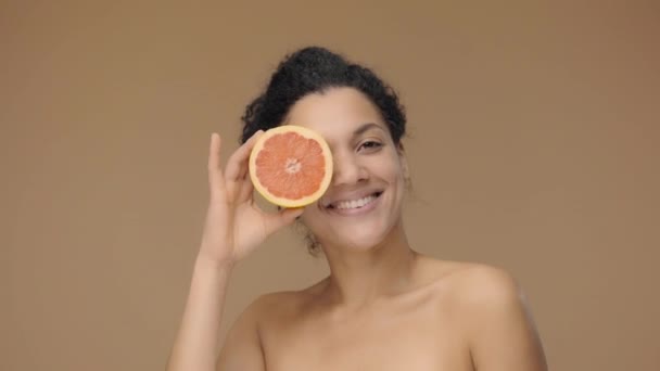 Schönheitsporträt einer jungen Afroamerikanerin, die sich mit einer halben Grapefruit vergnügt und ihr Aroma genießt. Schwarze Hündin auf braunem Studiohintergrund. Zeitlupe bereit, 4K bei 59.94fps. — Stockvideo