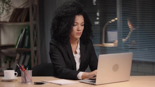 Portret van Afro-Amerikaanse vrouw in zakenpak die intensief typt op laptop. Zakenvrouw poseren op het werk, zitten aan tafel in het interieur van het kantoor. Slow motion klaar, 4K bij 59,94fps. — Stockvideo