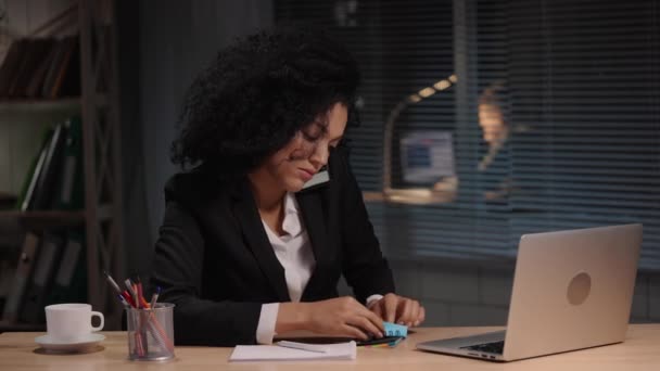 Portret van een Afro-Amerikaanse vrouw die praat op een smartphone en notities maakt op papier. Zakenvrouw poseert op het werk, zit aan tafel in functie. Slow motion klaar, 4K bij 59,94fps. — Stockvideo