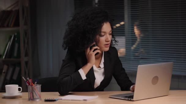 Porträt einer Afroamerikanerin im Businessanzug, die mit dem Smartphone spricht. Geschäftsfrau posiert am Arbeitsplatz, sitzt am Tisch im Inneren des Büros. Zeitlupe bereit, 4K bei 59.94fps. — Stockvideo