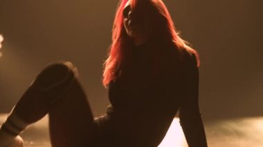 Flexible young woman moves her ass, dances twerk in a black leotard. Silhouette of an alluring dancer shaking her buttocks in a dark studio with bright lights. Close up.