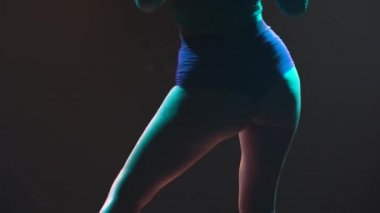 Seductive twerk dance performed by an alluring dancer in short shorts. Silhouette of a young woman twerking her ass while lying on the floor in a dark studio with bright lights. Close up.