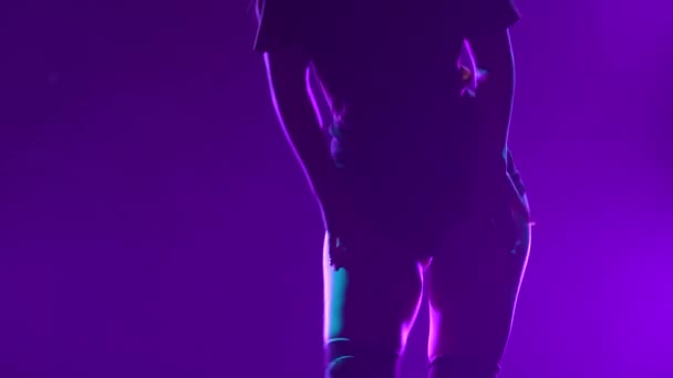 O siluetă a unei dansatoare seducătoare care își mișcă șoldurile și își răsucește fundul într-un studio întunecat cu lumini violet. O tânără atrăgătoare dansează twerk și își flexează corpul sexual. Close up . — Videoclip de stoc