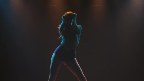 Seductive twerk dance performed by an alluring dancer in short shorts. Silhouette of a young woman twerking her ass in a dark studio with bright lights. Slow motion. — Vídeo de Stock