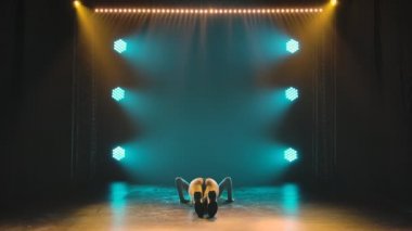 Silhouette of slim athletic woman shaking her ass while sitting on floor in dark studio with blue lights. Dancer twerks seductively and demonstrates flexibility of her sexy body. Slow motion.