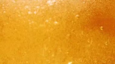 Bira köpüklü makro. Yakınlarda hafif bira bardağının içeriği var. Altın sıvı bardağa dökülüyor, kabarcıklar, dalgalar ve girdaplara neden oluyor. Taze bira, alkollü içecek. Yavaş çekim.