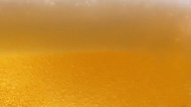Bardakta light bira makrosu. İnce bir altın sıvı damlası bardağa dökülerek birçok kabarcık, dalga ve köpük oluşturur. Taze demlenmiş alkollü içecek birası. Yakın plan. Yavaş çekim.