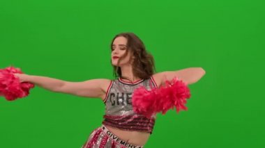 Ponpon kız coşkulu bir ponpon dansı yapar ve kalçalarını oynatır. Kız yeşil ekranda stüdyodaki takım yarışmasına hazırlanıyor. Kapatın. Yavaş çekim.