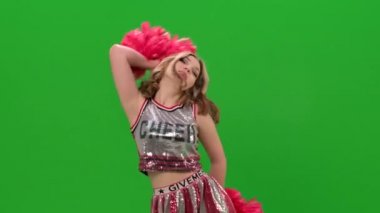 Kırmızı ponponlu kırmızı üniformalı bir kız stüdyoda yeşil ekranda dans ediyor. Dans, akrobasi, jimnastik, senkronize hareket. Kapatın. Yavaş çekim.