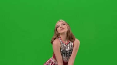 Çekici bir ponpon kız neşe içinde dans ediyor, kalçalarını hareketli bir şekilde sallıyor, daireler çiziyor, öpücük savuruyor. Dans, akrobasi, jimnastik, senkronize hareket. Kapatın. Yavaş çekim.