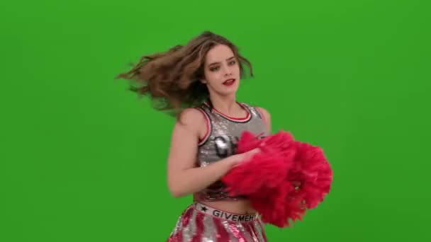 Een aantrekkelijke jonge cheerleader in uniform voert een jubelende dans uit met rode pompons in de studio op een groen scherm. Sluiten.. — Stockvideo