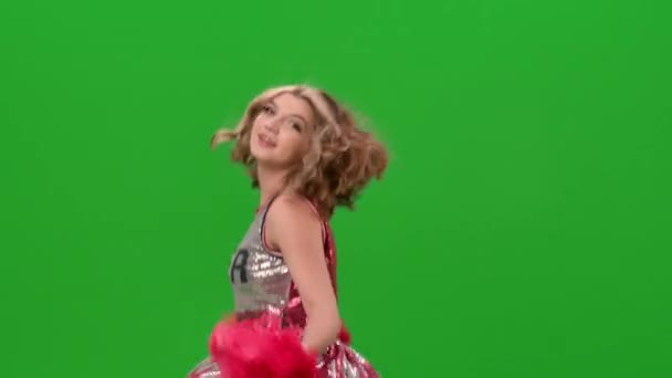 Une adorable pom-pom girl en uniforme avec des pompons rouges exécute une danse jubilatoire. Portrait d'une jeune femme souriante dansant en studio sur un écran vert. Ferme là. Mouvement lent. — Video