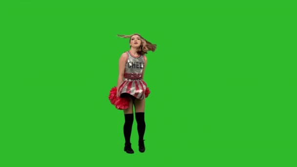 Uma adorável líder de torcida de uniforme com pompons vermelhos realiza uma dança jubilosa. Retrato de uma jovem mulher sorrindo dançando no estúdio em uma tela verde. Movimento lento. — Vídeo de Stock
