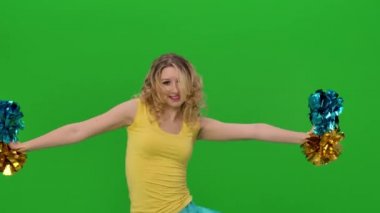 Amigo kız kalçalarını, ponpon kollarını, kıvırıp saçlarını sallıyor. Sarı-mavi üniformalı bir kız stüdyoda yeşil ekranda coşkulu bir dans ediyor. Kapatın. Yavaş çekim.