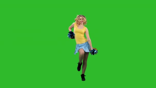 Een cheerleader beweegt krachtig haar heupen, pompoenarmen, wervelt en zwaait met haar haar. Een meisje met een geel-blauw uniform danst een jubelende dans in de studio op een groen scherm. Langzame beweging. — Stockvideo