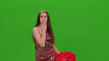 Stüdyoda kırmızı ponpon kızlarla yeşil ekranda dans eden mutlu bir ponpon kızın portresi. Çekici genç bir amigo kız dans ediyor ve öpücük yolluyor. Kapat..